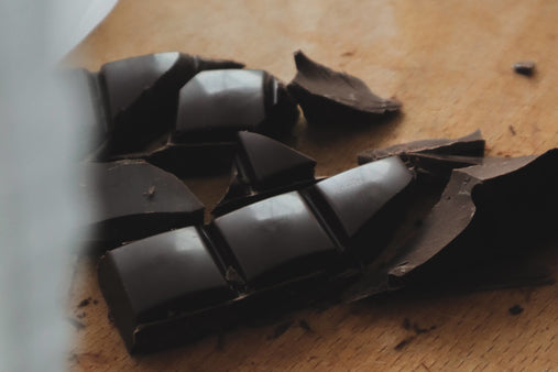A bar of dark chocolate is broken into pieces on a wooden surface