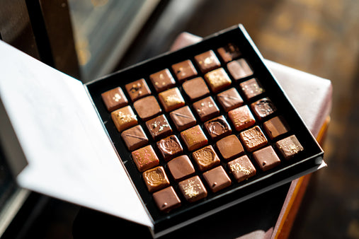A box of thirty six chocolate squares sits on a table in the center of the image